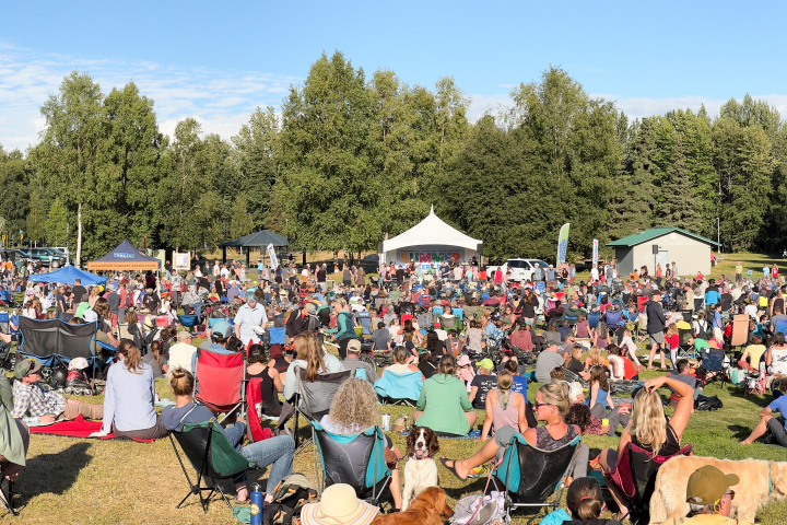 A crowd sits in the sun at Music in the Park. Chugach Electric's electric truck powers the event in the background.
