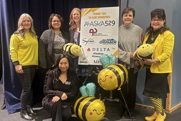 2026 Alaska Spelling Bee volunteers gather around a sponsorship poster.