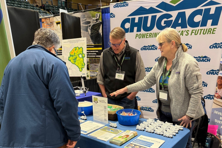 Chugach employees wearing badges speaker to a visitor at the booth