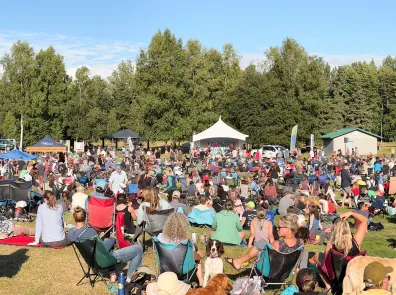 A crowd sits in the sun at Music in the Park. Chugach Electric's electric truck powers the event in the background.