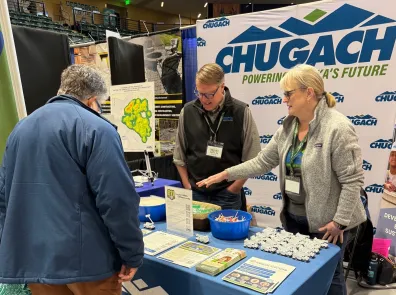 Chugach employees wearing badges speaker to a visitor at the booth