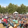 A crowd sits in the sun at Music in the Park. Chugach Electric's electric truck powers the event in the background.