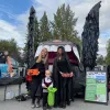 Two women and a child, all dressed as vampires, stand in front on an electric vehicle's frunk that is decorated to look like a vampire bat.