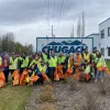 Employees in hi-vis vests pose by the Chugach sign with trash picker tools and orange Citywide Cleanup garbage bags.