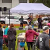 A crowd watches musicians perform under a white tent at an outdoor event. A Chugach Electric RV truck is parked behind them.