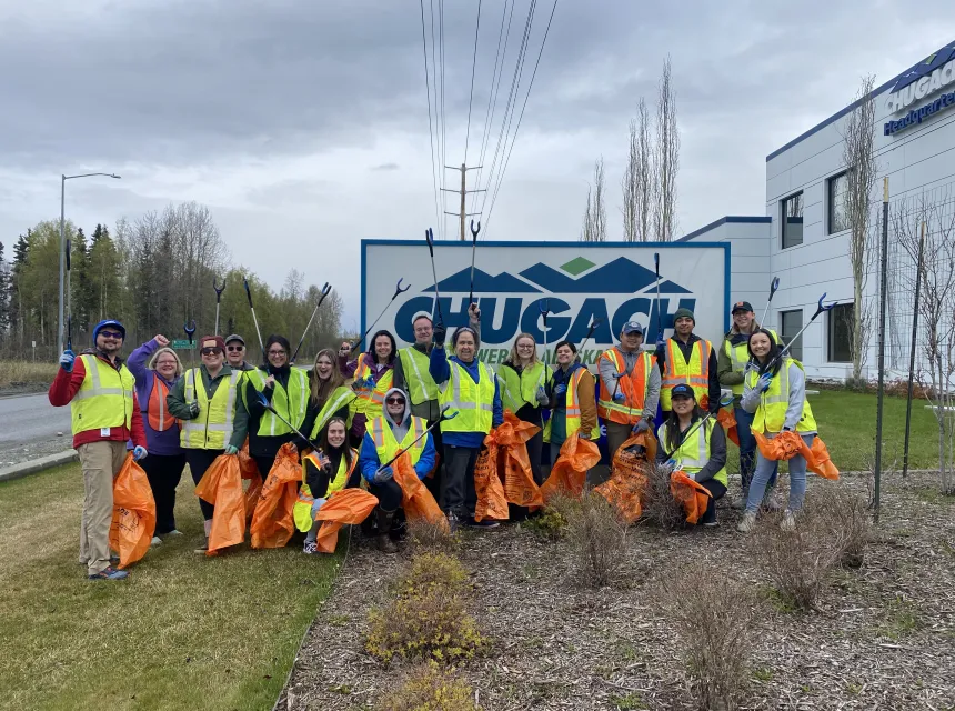 Employees in hi-vis vests pose by the Chugach sign with trash picker tools and orange Citywide Cleanup garbage bags.