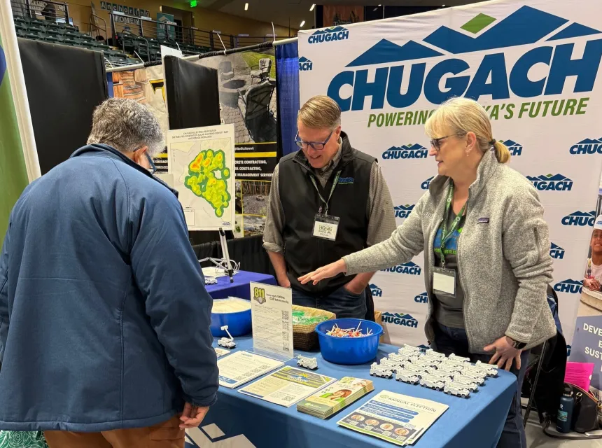 Chugach employees wearing badges speaker to a visitor at the booth