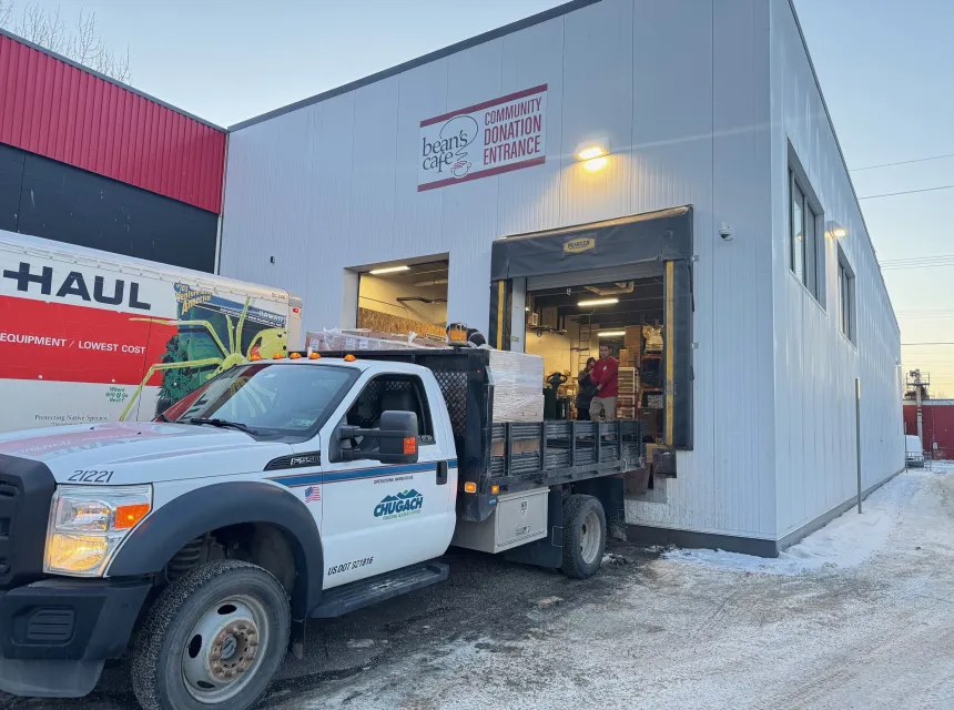 A Chugach Electric truck loaded with boxes of frozen turkeys pulled up to the loading dock at Bean's Cafe. A sign above the door says, "Community Donation Entrance" and people can be seen unloading the truck.
